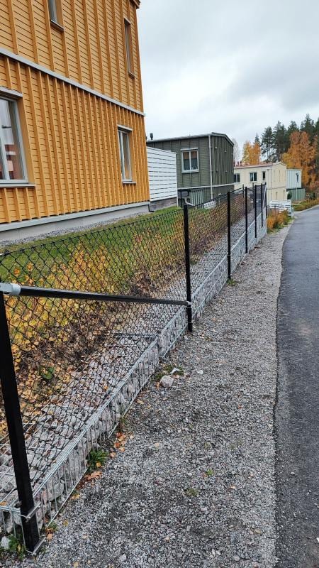 Svart flätverksstängsel som följer markens lutning längs en gångväg.