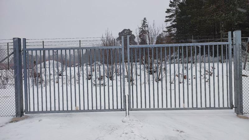 Dubbel slaggrind med stående stålprofiler och anslutande flätverksstängsel.